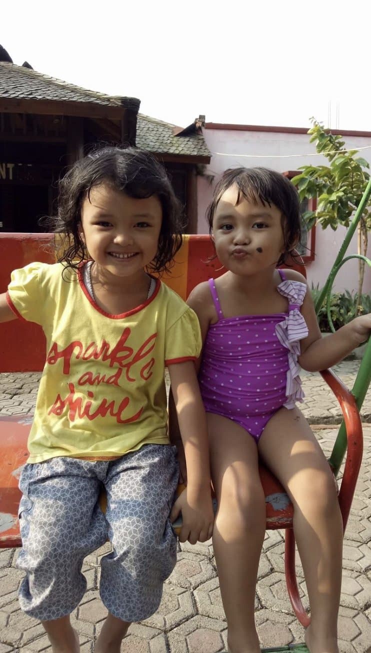 Two young girls in Indonesia smiling on a bench